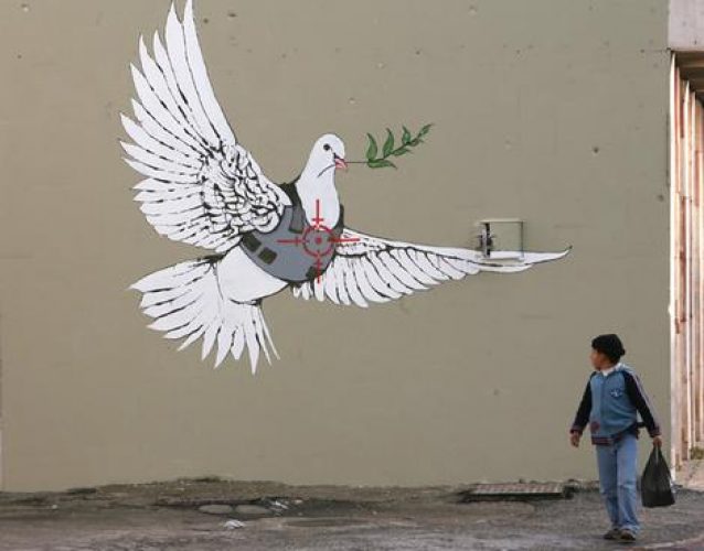 A Palestinian boy looks at one of six new images painted by British street artist Banksy as part of a Christmas exhibition in the West Bank town of Bethlehem